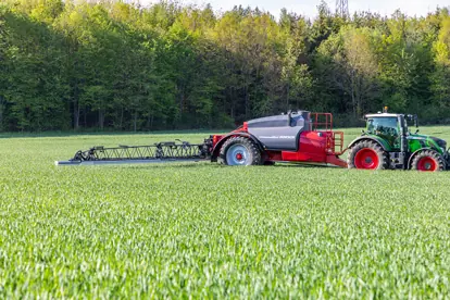 Ein Traktor mit Spritzgerät bearbeitet ein grünes Feld, symbolisch für moderne Agrartechnik in der Landwirtschaft.