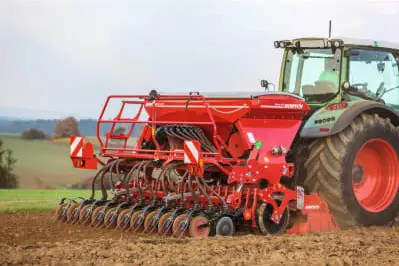 Eine moderne Agrartechnik-Maschine bearbeitet den Boden auf einem Feld mit Blick auf eine ländliche Landschaft.