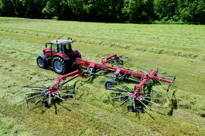 Ein Traktor mit einer großen Heuwender-Ausrüstung bearbeitet ein Feld im Bereich Agrartechnik.