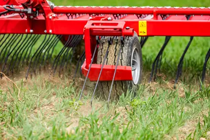 Eine rote Agrartechnik-Maschine bearbeitet den Boden mit einem rotierenden Rechen in einem grünen Feld.