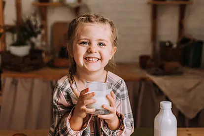 Ein glückliches Mädchen hält ein Glas Milch, das die positive Einstellung zu Milch gesund unterstreicht.