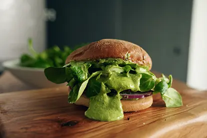 Ein frischer Burger mit Salat und grünem Dressing, präsentiert auf einem Holzbrett, ideal für saisonale Rezepte.