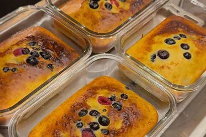 Goldgelber Protein-Quark-Auflauf mit Beeren in vier Glasformen frisch aus dem Ofen.