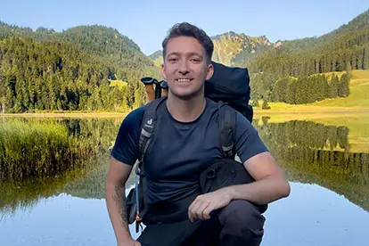 Aktiver Mann mit Rucksack vor malerischem Bergsee, symbolisiert Abenteuer und Naturverbundenheit für Hafer-Heidel-Power-Boost.