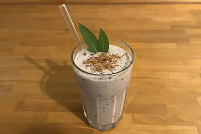 Ein cremiger Hafer-Heidelbeer-Smoothie in einem Glas mit Strohhalm und dekorativen Blättern auf einem Holztisch.