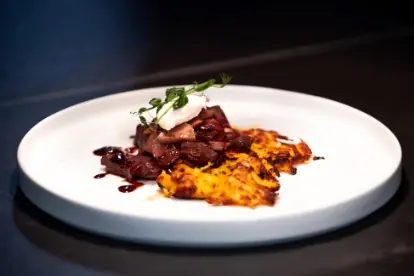 Blitz Boeuf Bourguignon mit Kartoffel-Kürbis Rösti, garniert mit Kräutern und einem Klecks Sahne auf einem weißen Teller.
