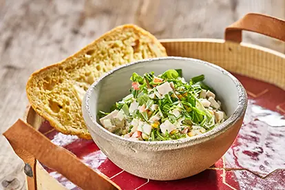 Eine Schüssel mit Putenbraten, frischem Gemüse und Kräutern, serviert mit einem Stück Brot auf einem rustikalen Tablett.