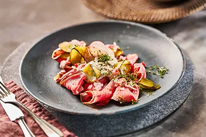 Saftiges Roastbeef mit Gewürzgurken und Kräutern auf einem eleganten Teller, serviert auf einem rustikalen Untersetzer.