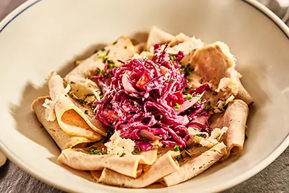 Zarte Scheiben Schweinebraten mit roten Zwiebeln, Sauerkraut und frischen Kräutern in einer Schüssel angerichtet.