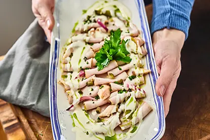 Zarte Kalbsfleischscheiben mit einer cremigen Sauce, garniert mit Petersilie und Zwiebeln auf einem Servierteller.