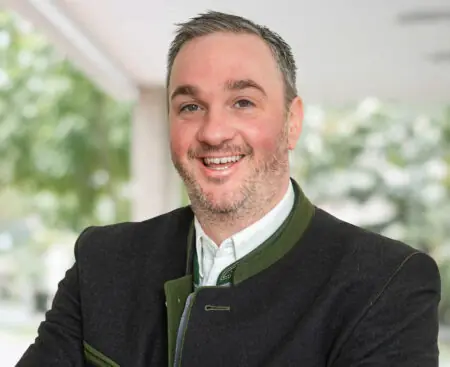 Andreas Gasteiger, Agrardirektor der meine Volksbank Raiffeisenbank eG in Rosenheim, lächelnd mit verschränkten Armen im Trachtenjanker. Sponsor von Unsere Bayerischen Bauern.