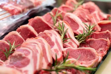 Rohe Schweinekoteletts mit Fettrand, dekorativ auf einer Fleischtheke angeordnet und mit Rosmarinzweigen garniert